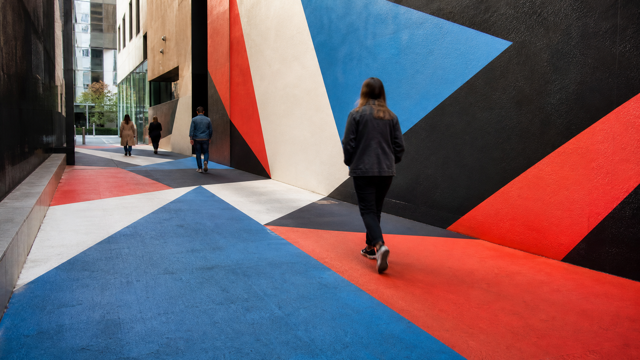Pedestrians moving through a city passage where bold painted forms connect wall and ground surfaces